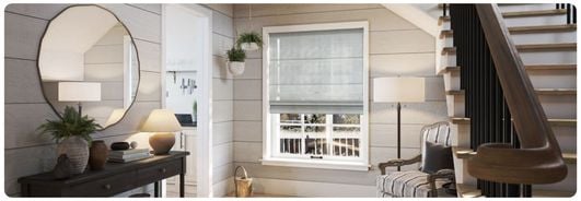 A sheer/voile grey Roman blind over a sash window in a grey, panelled hallway