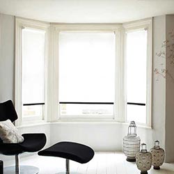 Inside a living room, the view is an angled bay windows with white and black blinds in them.