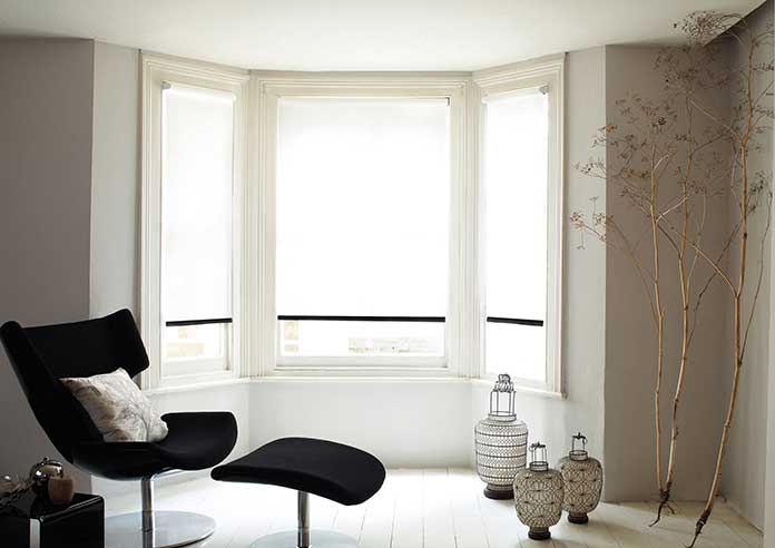 Inside a living room, the view is an angled bay windows with white and black blinds in them.