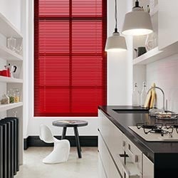 A red aluminium venetian in a window. The kitchen is white, black and modern in style.