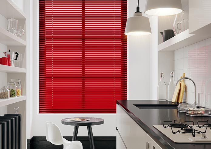 A red aluminium venetian in a window. The kitchen is white, black and modern in style.