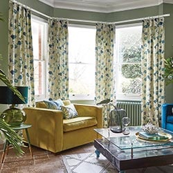 Floral green and blue curtains adorn a bay window in a green living room.