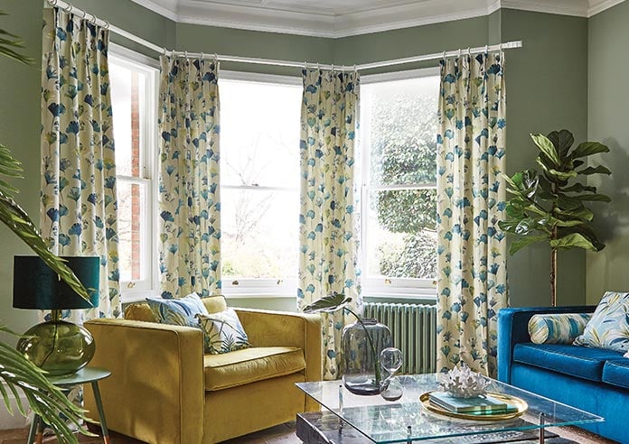 Floral green and blue curtains adorn a bay window in a green living room.
