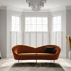 White shutters in a living room. An orange sofa is in front of the bay window.