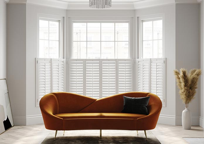 White shutters in a living room. An orange sofa is in front of the bay window.