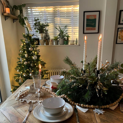 Christmas table decorations in a dining room featuring white wooden Venetian blinds.