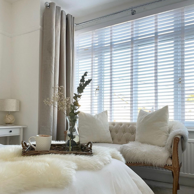 White wooden blinds layered with brown curtains shown in a bedroom