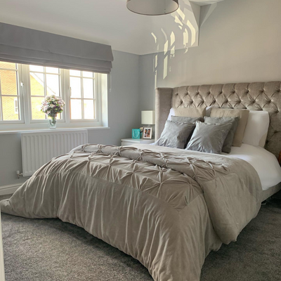 A bedroom featuring taupe Roman blinds and a bed decorated with pillows and throws.