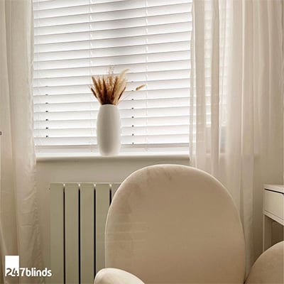 White faux wooden blinds shown in neutral room with sheer voile drapes.
