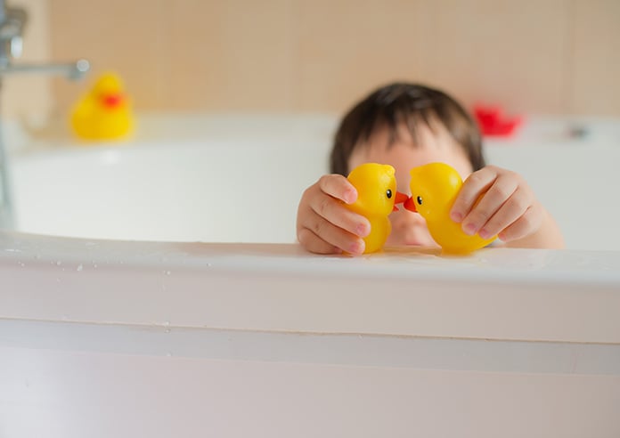 Little kid playing with toy ducks in a bubble bath