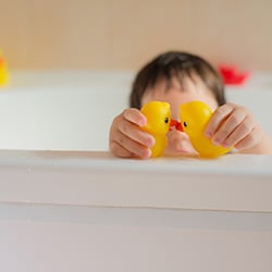 Little kid playing with toy ducks in a bubble bath