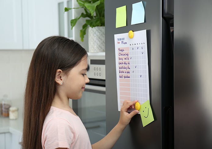 A young girl marking off her task list on the fridge
