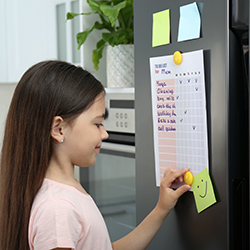 A young girl marking off her task list on the fridge