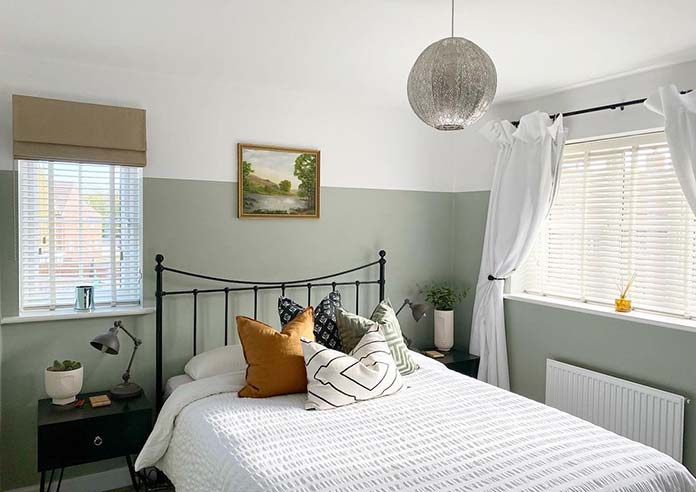 An image showing a bedroom with wooden blinds in the windows and a roman blind and curtains covering outside the recess