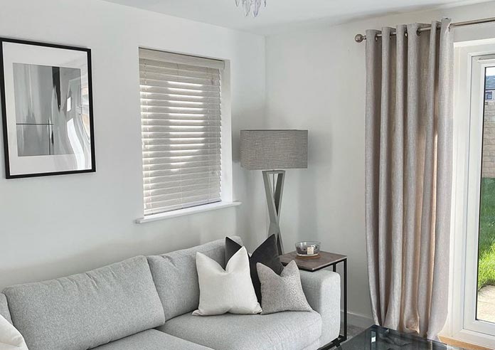 An image showing a living room with a wooden blind in a side window and eyelet curtains covering the french doors