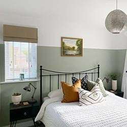 An image showing a bedroom with wooden blinds in the windows and a roman blind and curtains covering outside the recess