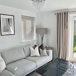 An image showing a living room with a wooden blind in a side window and eyelet curtains covering the french doors