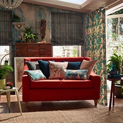 A bright botanical conservatory is shown with a ruby red sofa in the centre. The theme is tropical.