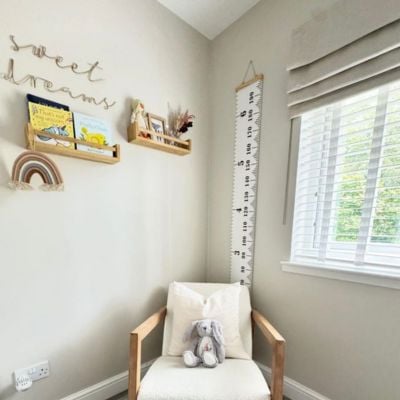 A beige roman blind layered over white wooden blinds in a neutral nursery 