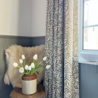White and green patterned, botanical curtains hung in a room with a half green wall and picture rail. 