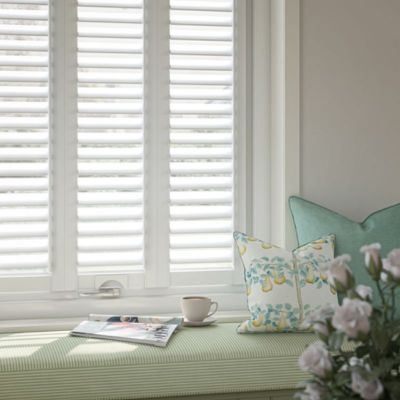 White no drill shutter blinds on a window next to a light green window seat.