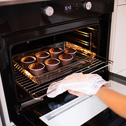 An image of a woman taking out buns from the oven