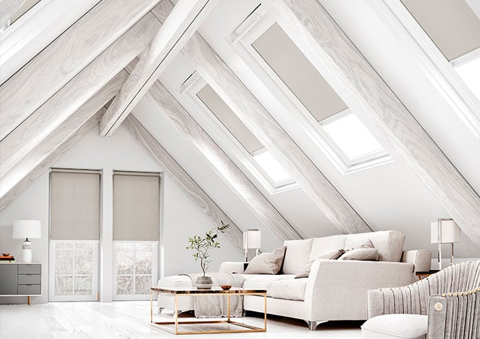 A select of grey blackout roller blinds show in a neutral white living room attic space.
